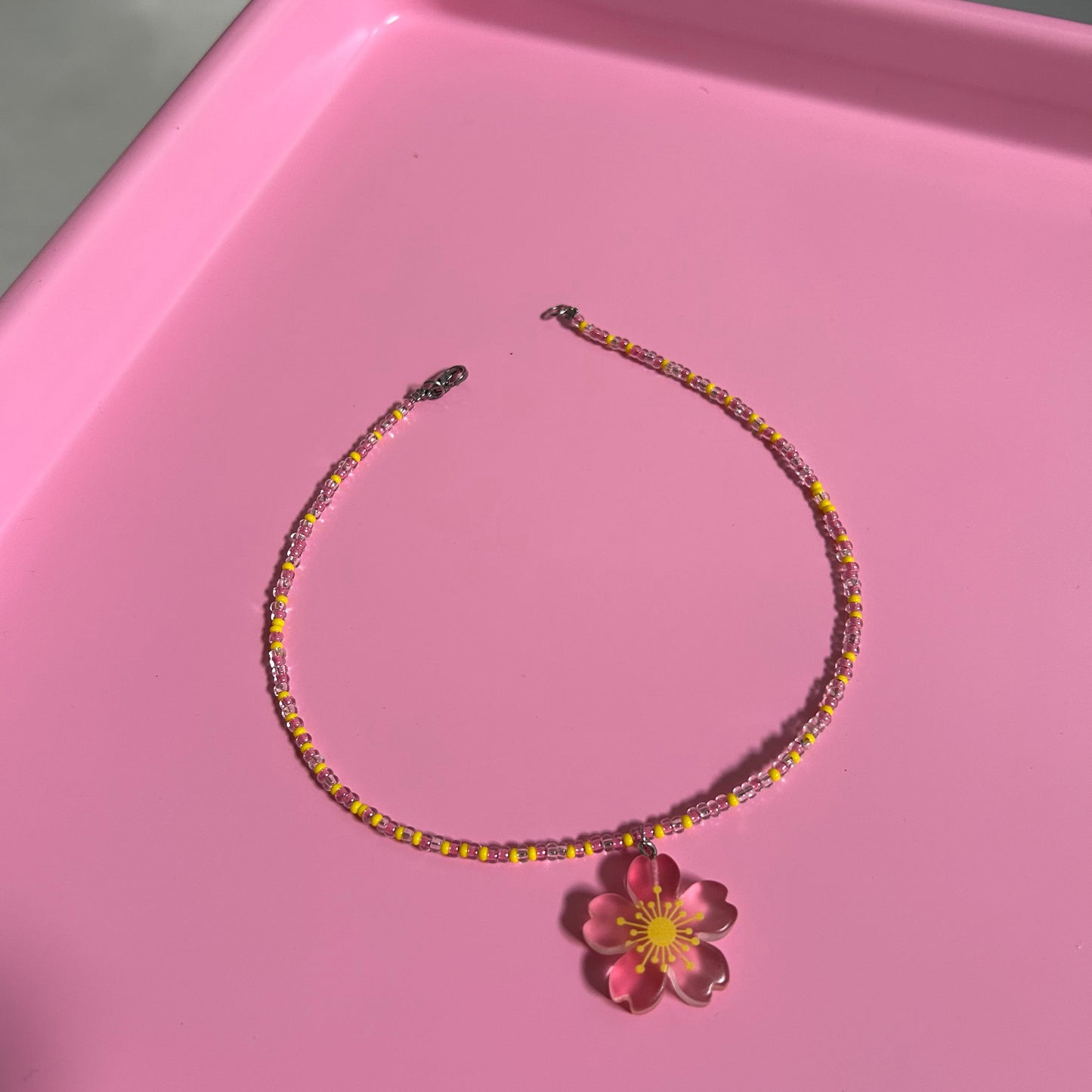 Beaded necklace with a flower accessory on a pink surface