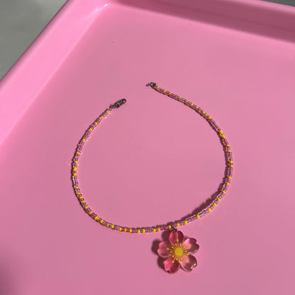 Beaded necklace with a flower accessory on a pink surface