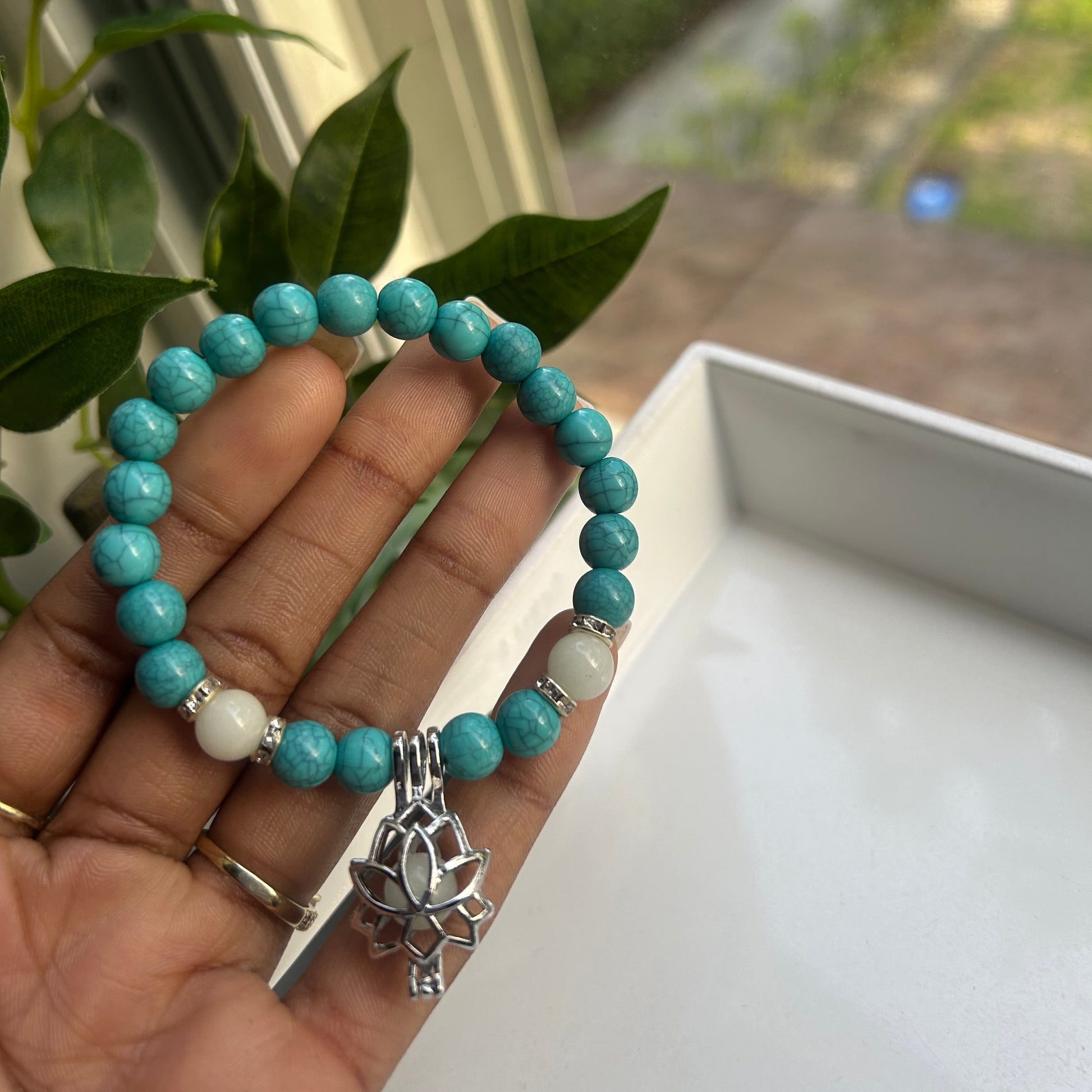 A turquoise beaded bracelet with white and silver accent beads and a silver turtle charm, held in a person's hand.