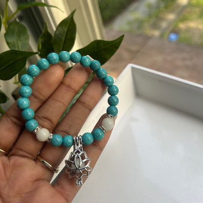 A turquoise beaded bracelet with white and silver accent beads and a silver turtle charm, held in a person's hand.