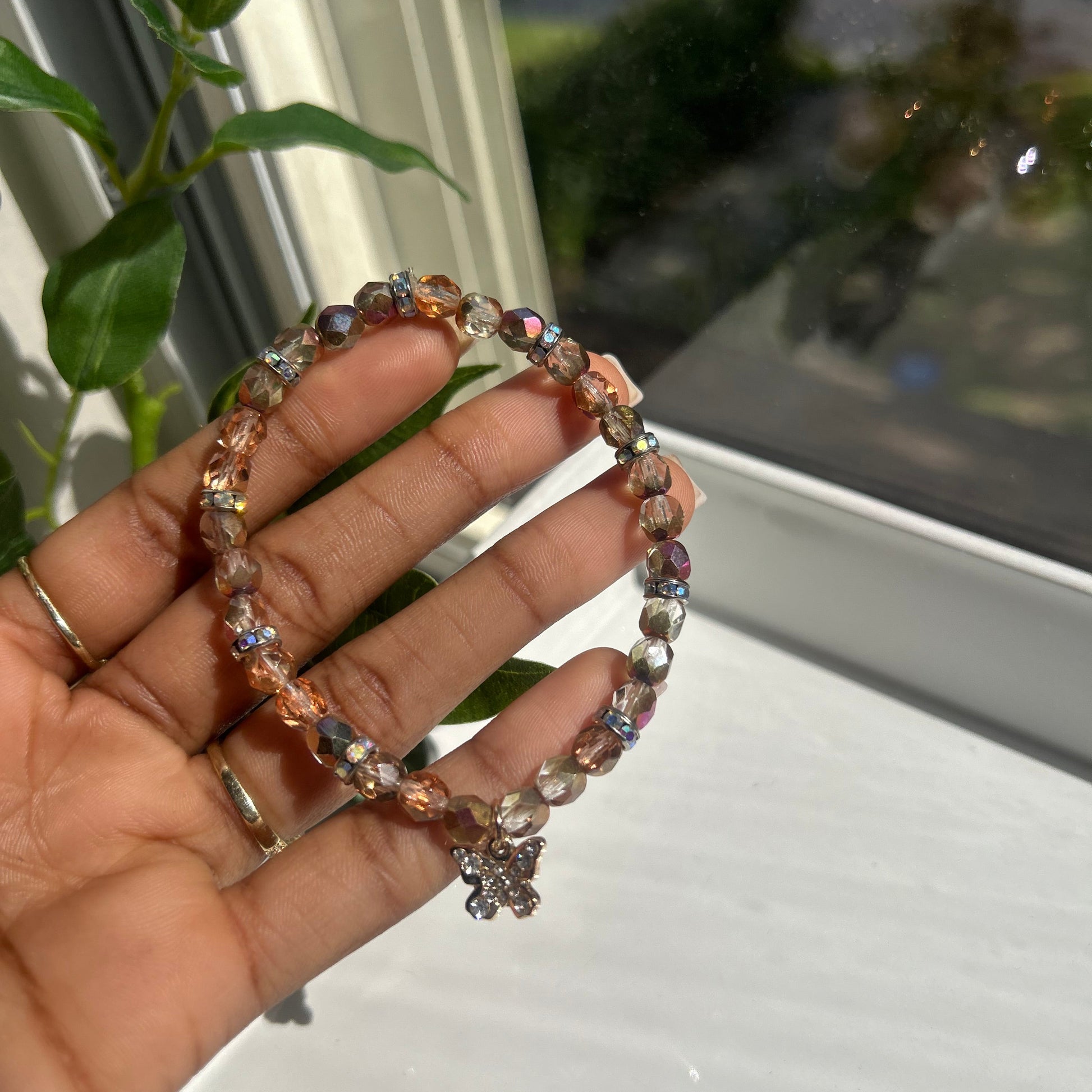 A beaded stretch bracelet with faceted rose gold and iridescent beads, held in a person's hand near a window.