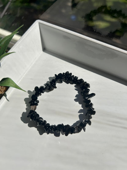 Black beaded bracelet on a white surface with a plant in the background