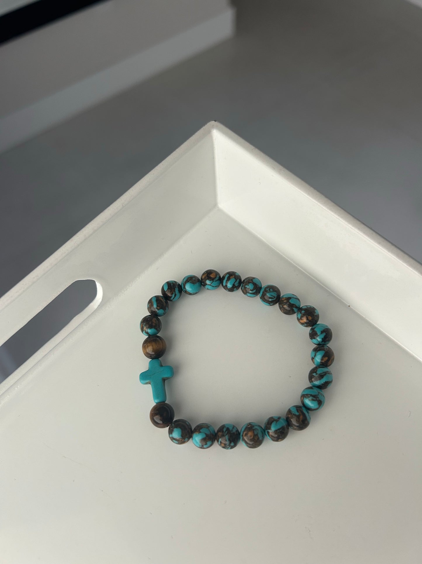 Turquoise and brown beaded bracelet with a cross charm on a white surface.
