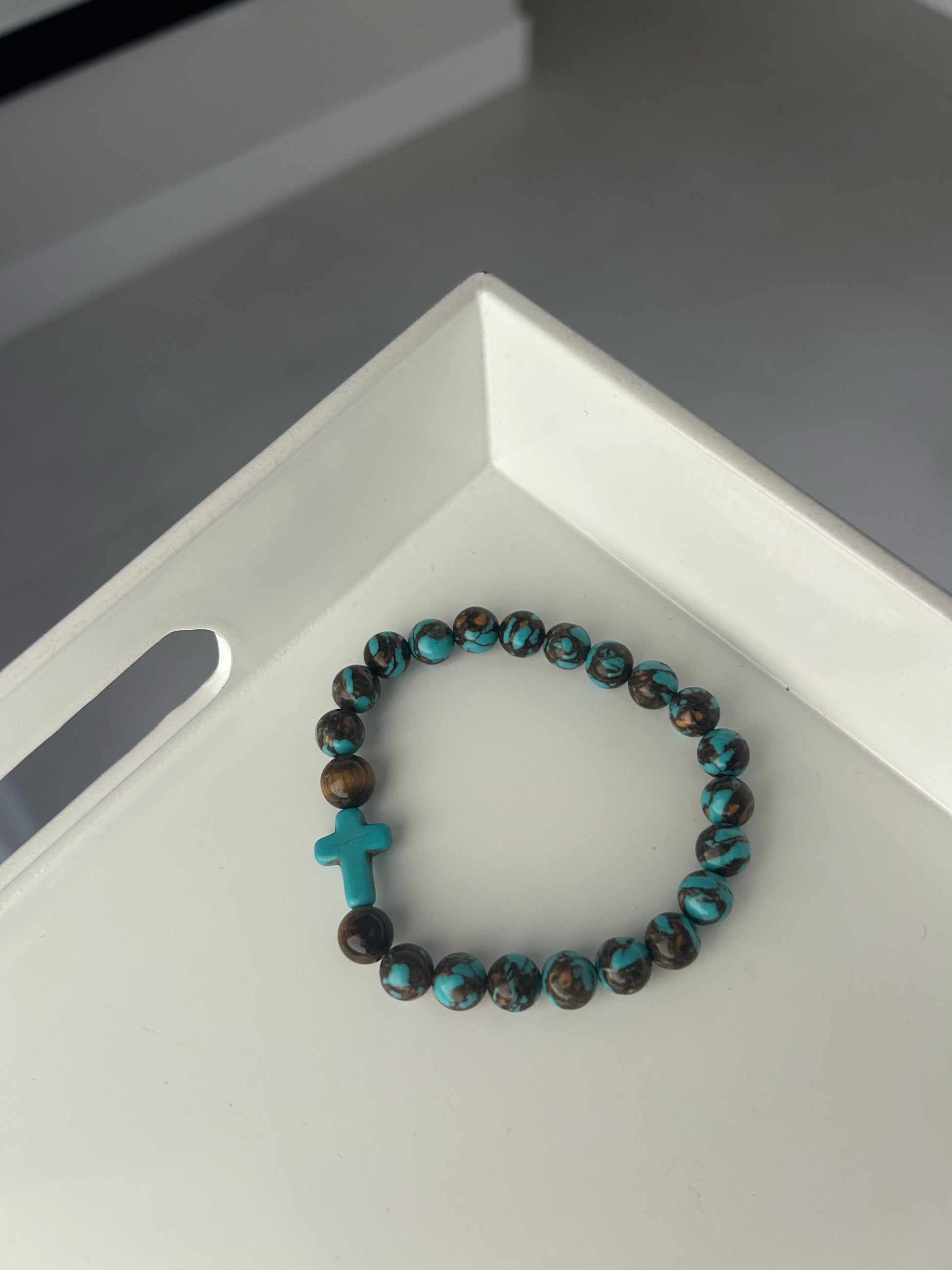 Turquoise and brown beaded bracelet with a cross charm on a white surface.