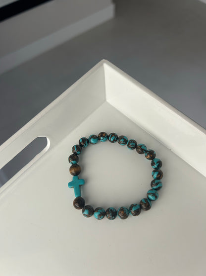 Turquoise and brown beaded bracelet with a cross charm on a white surface.