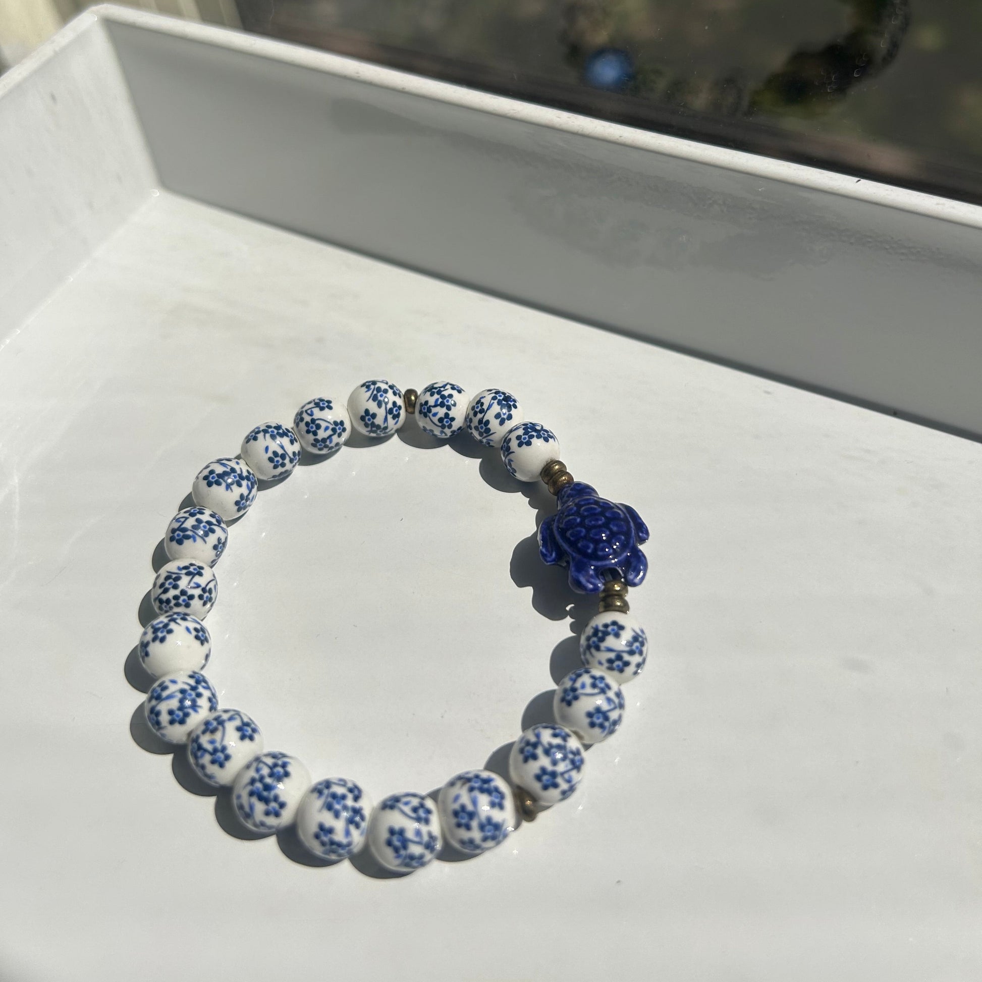 A beaded bracelet with white and blue patterned round beads and a central blue flower charm, displayed on a white surface.