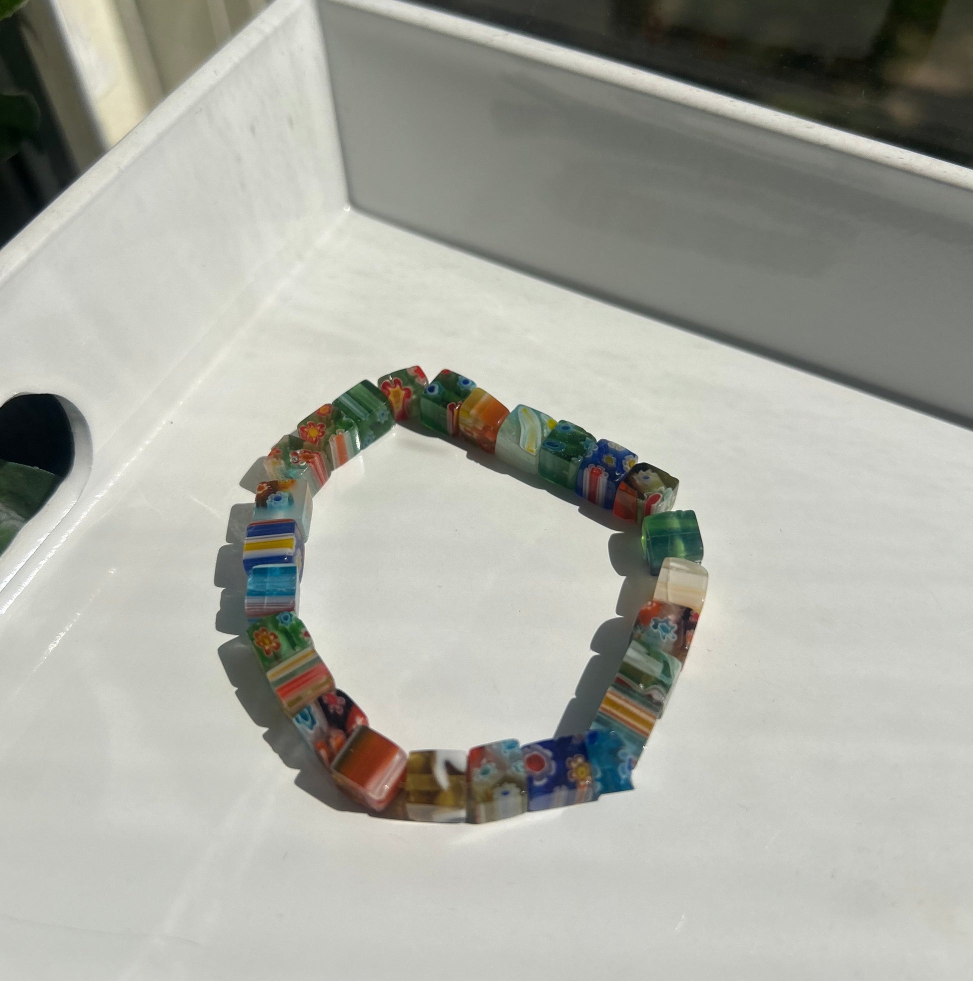 A circular beaded bracelet made of small colorful glass pieces, photographed resting on a white tray in natural light.