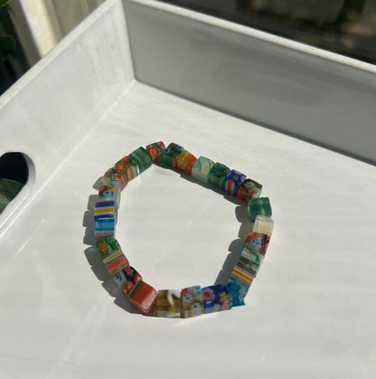 A circular beaded bracelet made of small colorful glass pieces, photographed resting on a white tray in natural light.