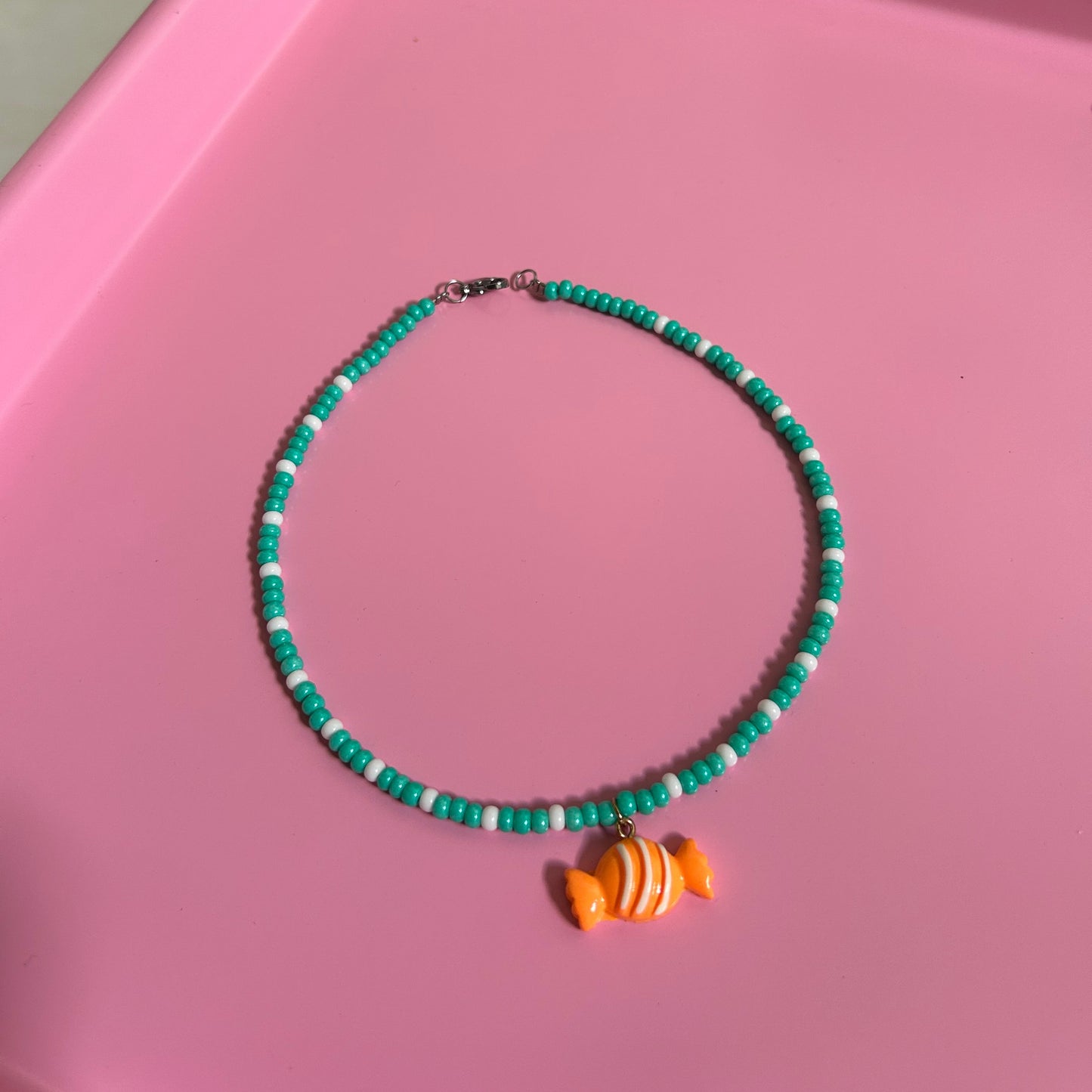 Green beaded necklace with an orange candy charm on a pink surface