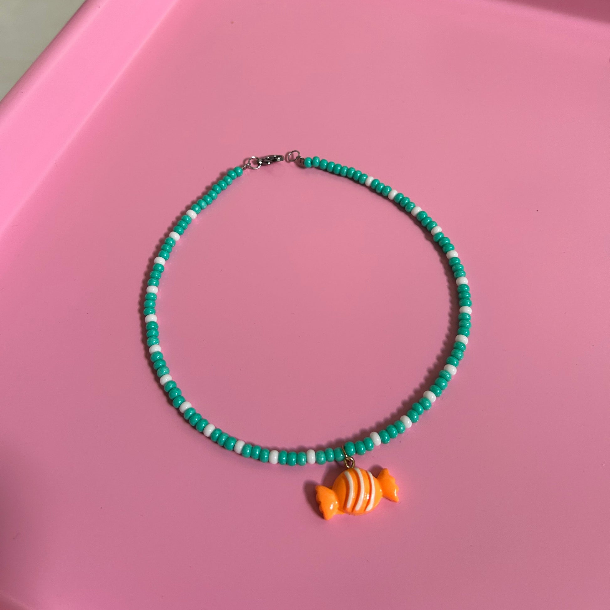 Green beaded necklace with an orange candy charm on a pink surface