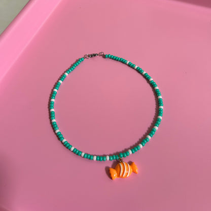 Green beaded necklace with an orange candy charm on a pink surface