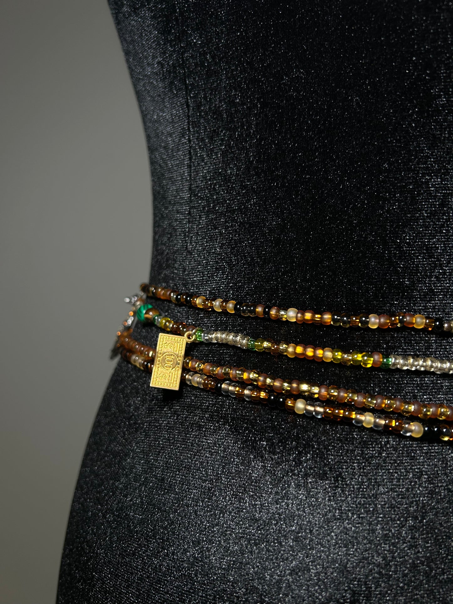 Three beaded waistbeads with a gold tag on a black background