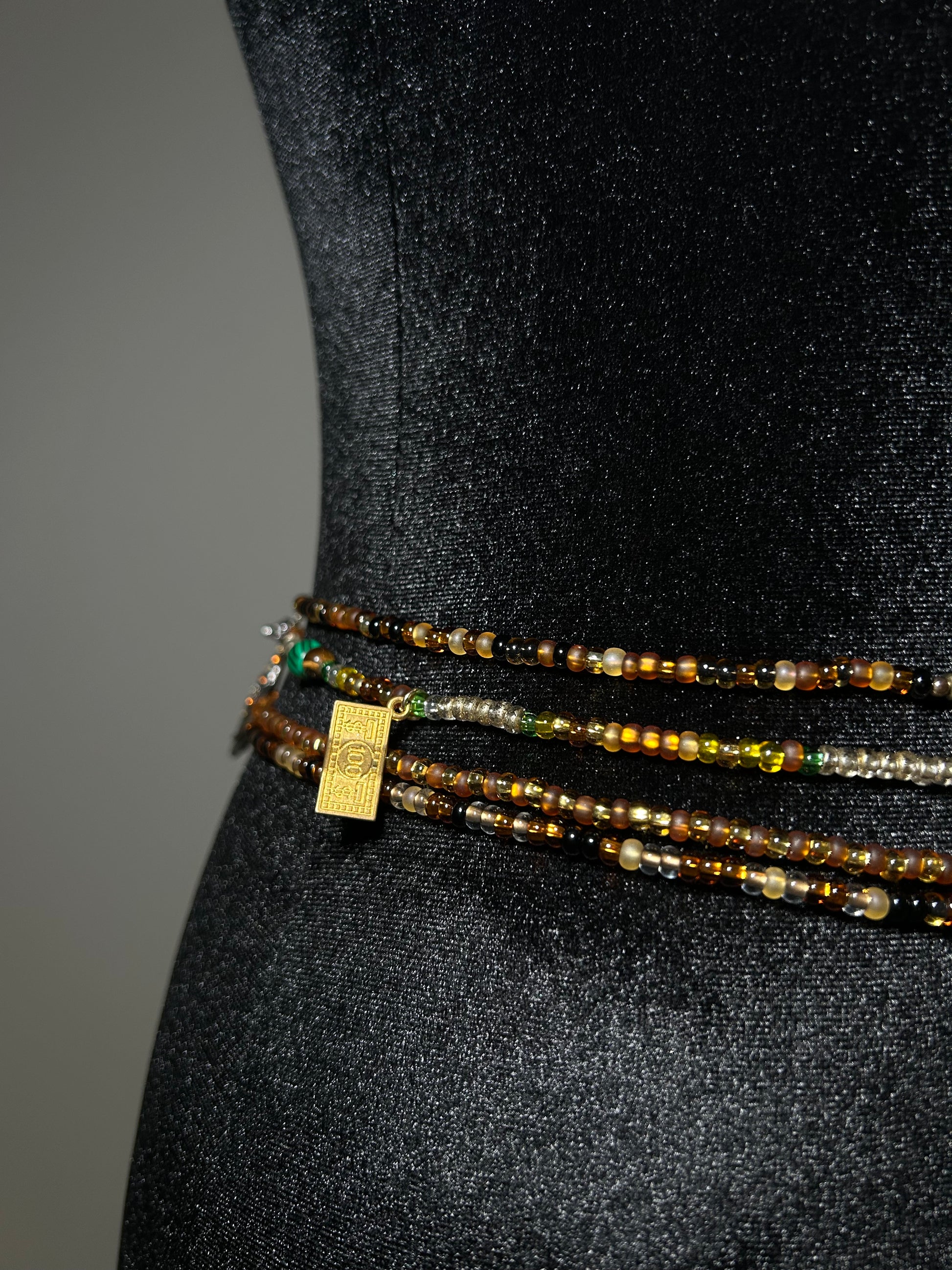 Three beaded waistbeads with a gold tag on a black background