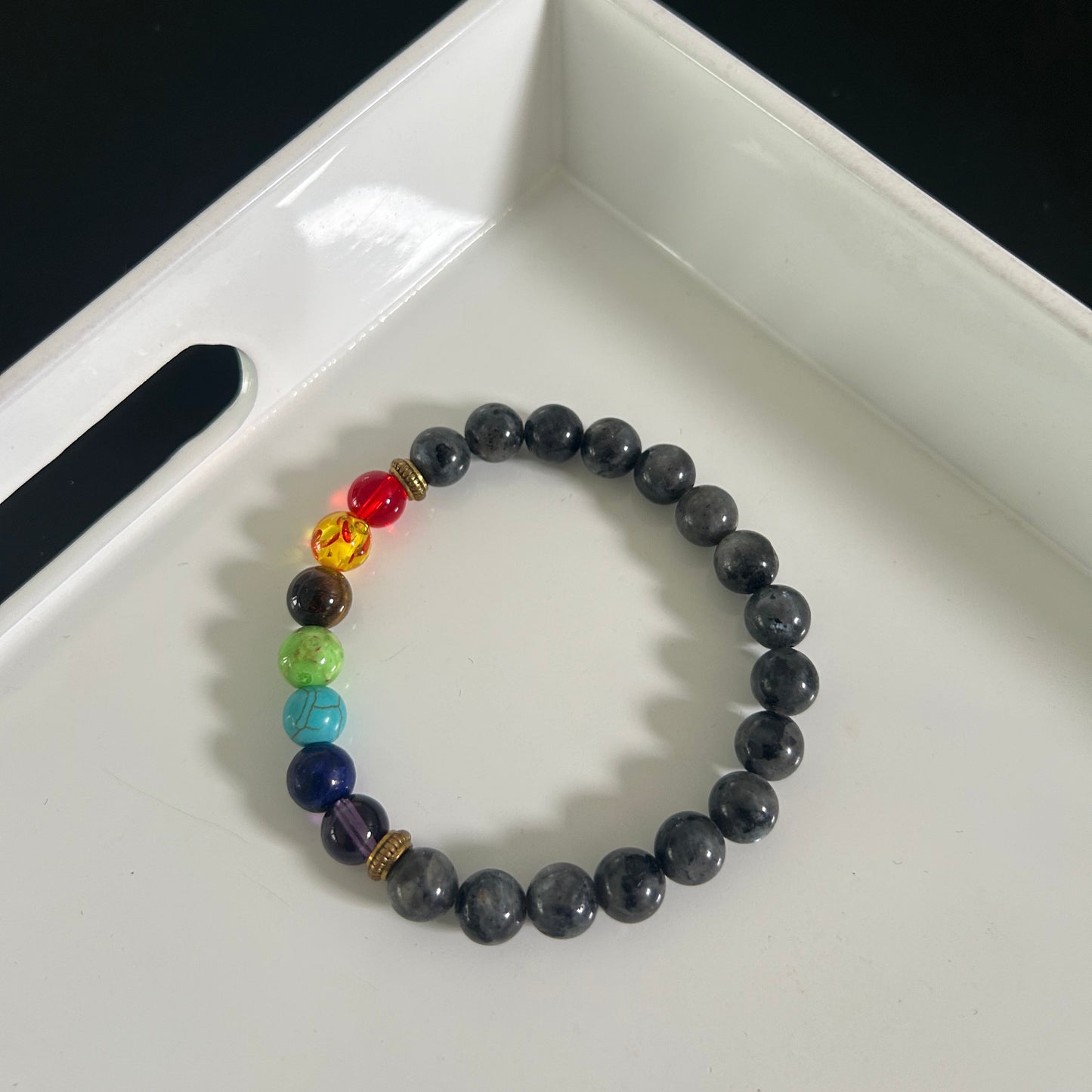 Black and grey beaded bracelet with colorful beads on a white tray