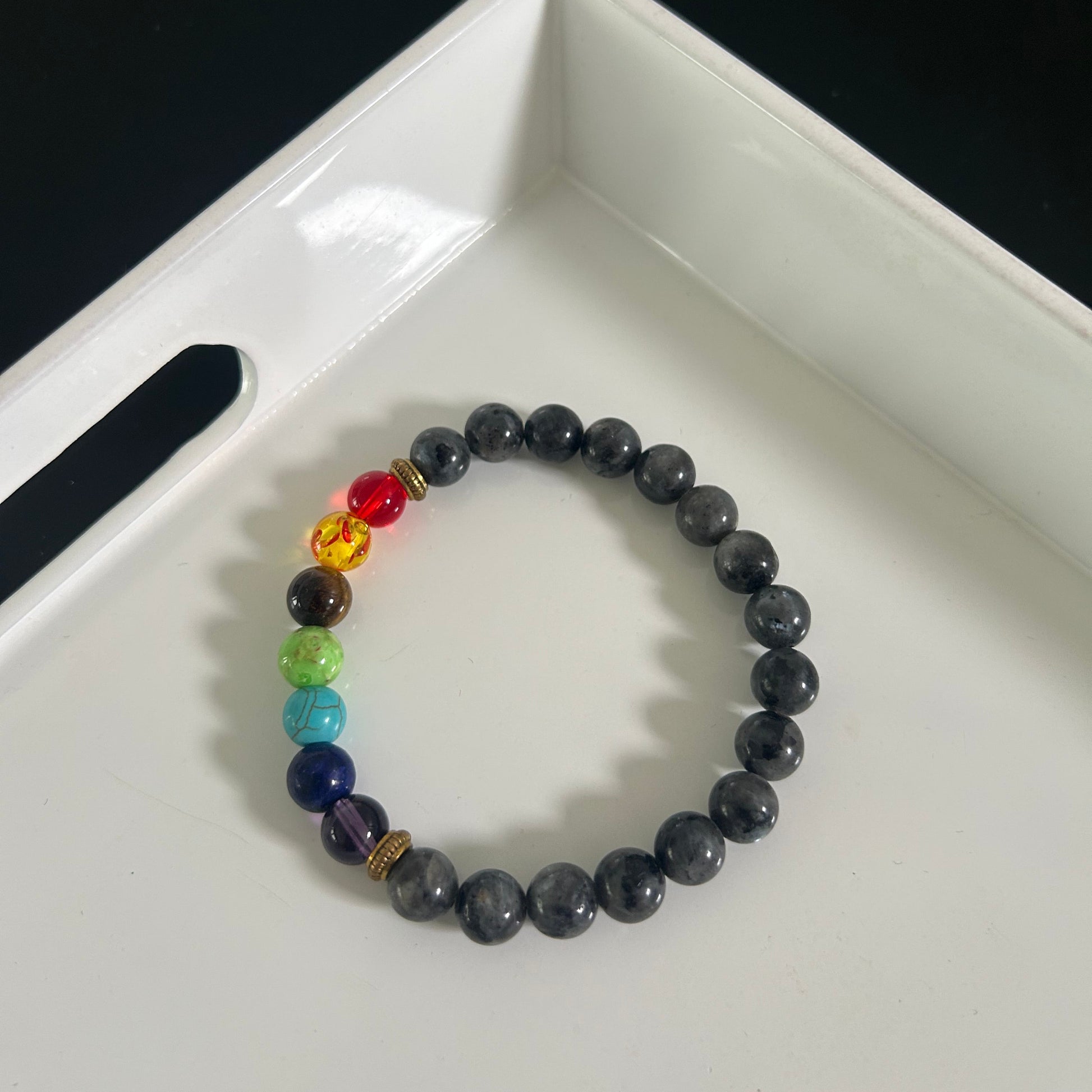 Black and grey beaded bracelet with colorful beads on a white tray