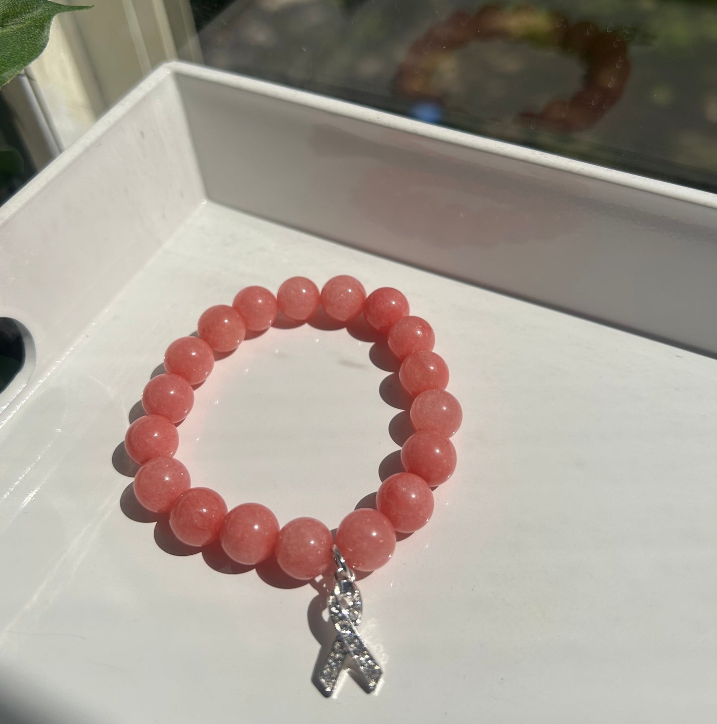 A pink beaded bracelet with a silver-toned butterfly charm, displayed on a white surface.