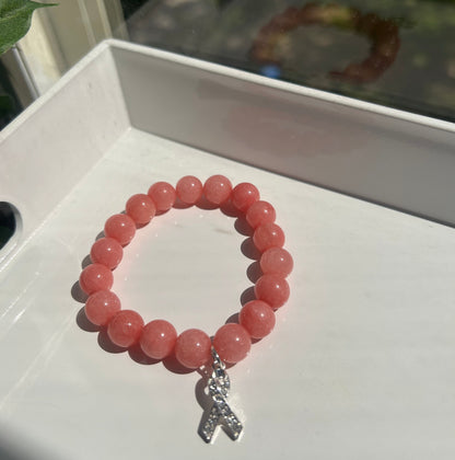 A pink beaded bracelet with a silver-toned butterfly charm, displayed on a white surface.