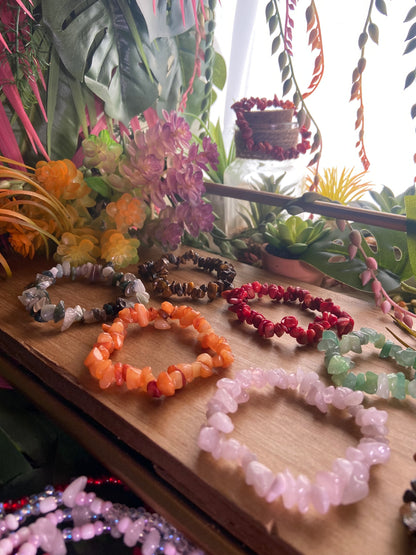 A collection of colorful bead bracelets displayed on a wooden surface, with various shades of beads and a few feathered accents.