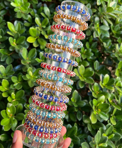 A multicolored gem bracelet displayed against a backdrop of greenery, with colors including blue, red, and gold.